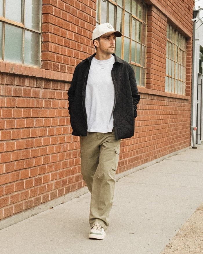 The Monterey Cargo Pant in light khaki — worn while walking along a red brick building