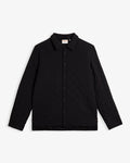 A front view of The Quilted Overshirt in black, laid flat on a white background. The image highlights the clean lines, signature wave quilting, and the c'est normal logo on the inner collar label.