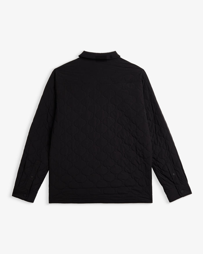 A back view of The Quilted Overshirt in black, laid flat on a white background. The image highlights the wave quilting pattern and the c'est normal logo embroidered on the upper back.