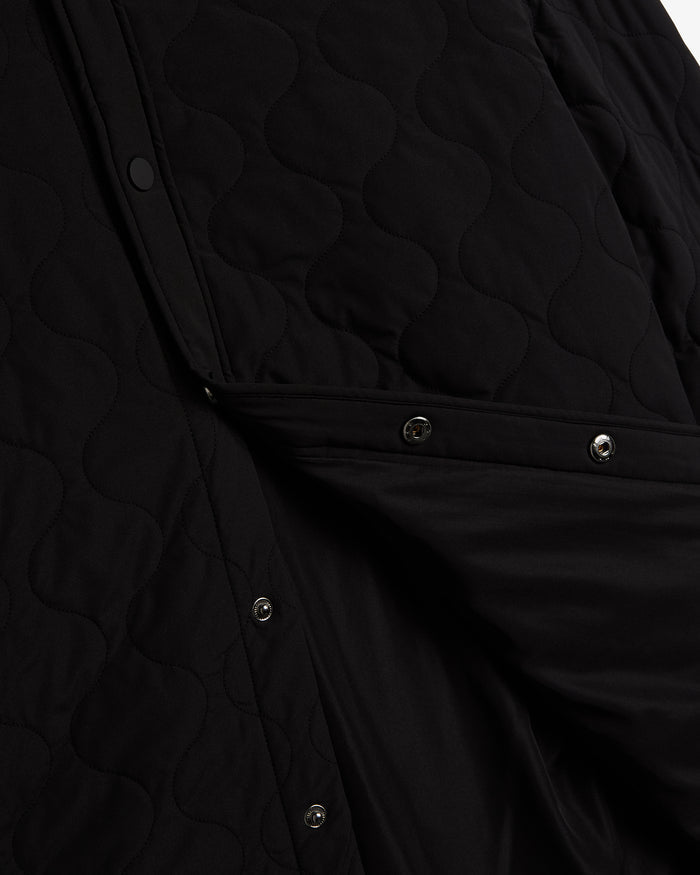 A close-up shot of The Quilted Overshirt in black, detailing the signature wave quilting and the metal snap buttons on the front closure.