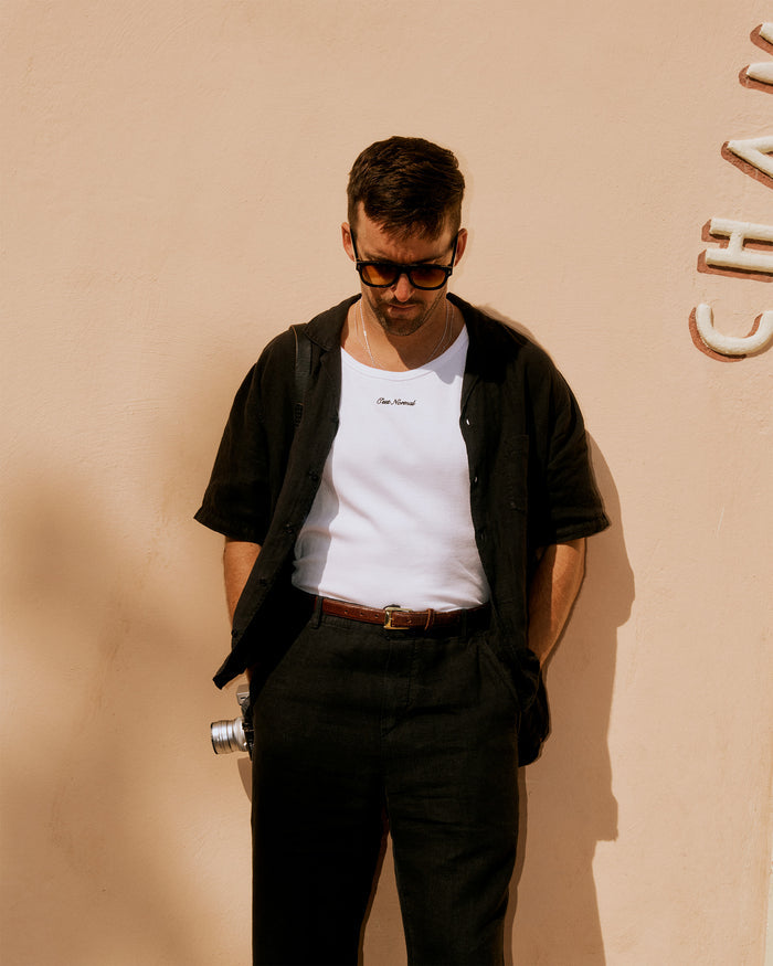 The Ribbed Tank Top in white — worn under an open black shirt with the C'est normal chest logo