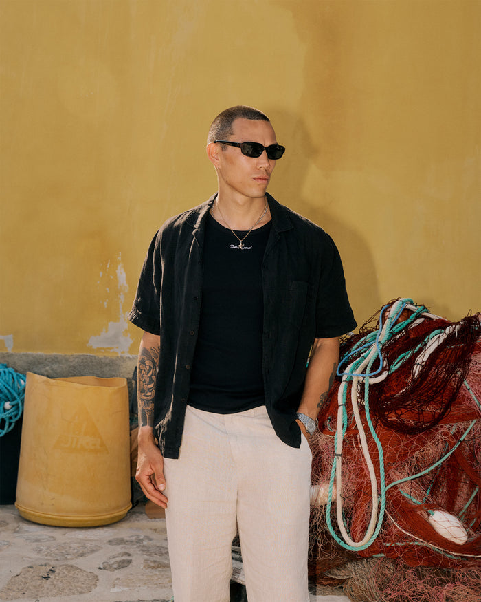 The Ribbed Tank Top in black — worn under an open black shirt next to fishing nets