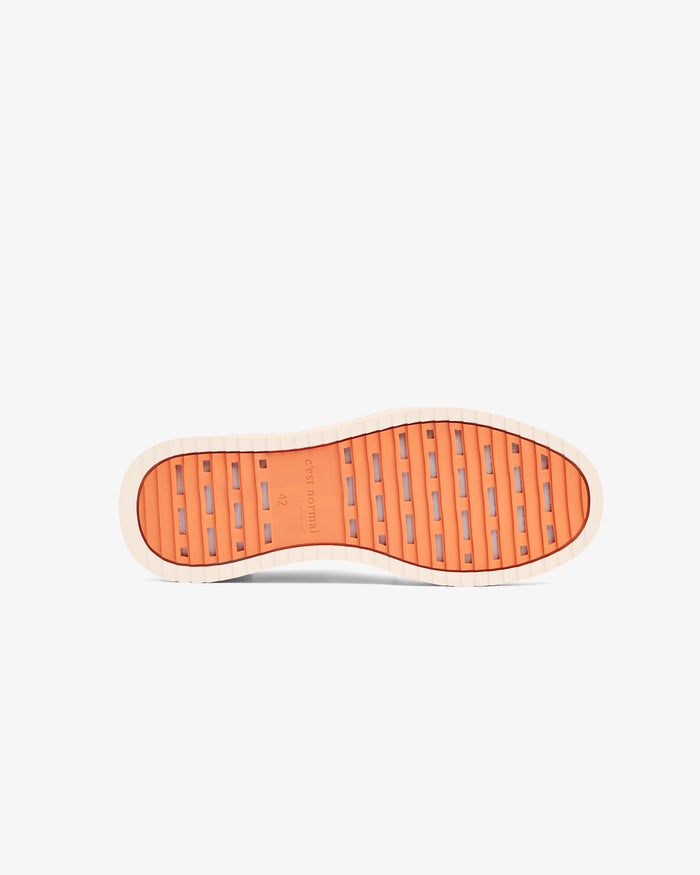 A bottom view of The Sneakers 2.0 in cream, laid flat on a white background. The image highlights the original orange EVA rubber grid sole featuring the c'est normal logo and size detailing in the center.