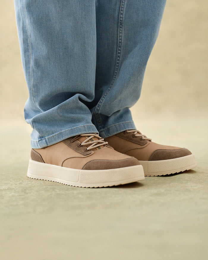 A close-up of a person wearing The Sneakers 2.0 Leather in sand leather and light blue jeans. The image highlights the tone-on-tone leather and suede upper and the thick white sole of the c'est normal sneakers.