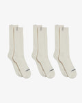 Three pairs of The Sock in cream, laid flat side-by-side on a white background. The image highlights the ribbed mid-calf design and the c'est normal logo on both the cuff tag and across the toe.