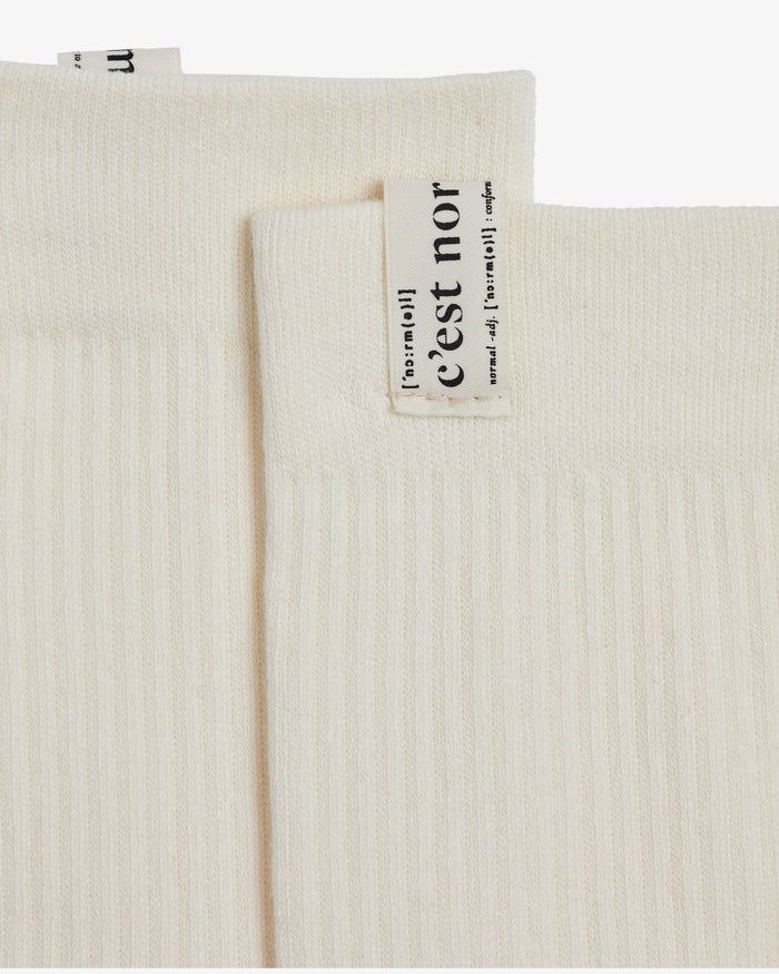 A close-up view of the ribbed fabric of The Sock Cream, focusing on the cuff tag featuring the c'est normal logo.