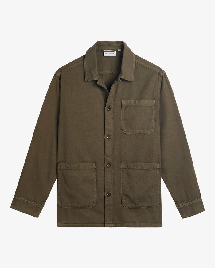 A front view of The Workwear Overshirt in olive green, laid flat on a white background. The image highlights the button-up front, patch pockets at the left chest and hips, and the c'est normal tag inside the collar.