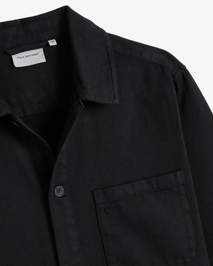 The Workwear Overshirt in black — close-up of the collar and chest pocket with subtle branding