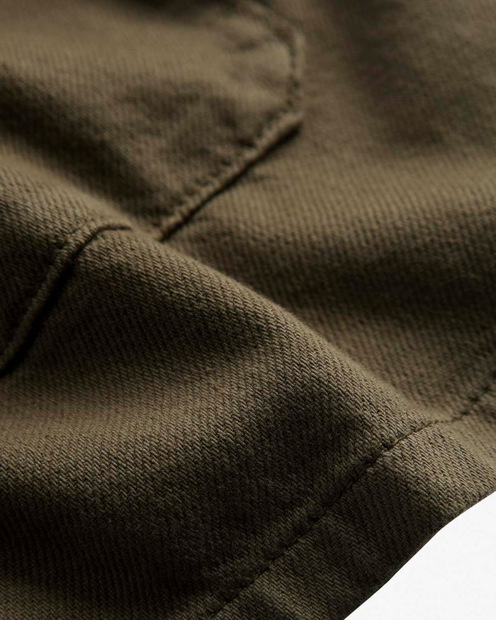 A detailed close-up shot of the textured cotton fabric of The Workwear Overshirt in Olive Green, showing the stitching and part of a pocket.
