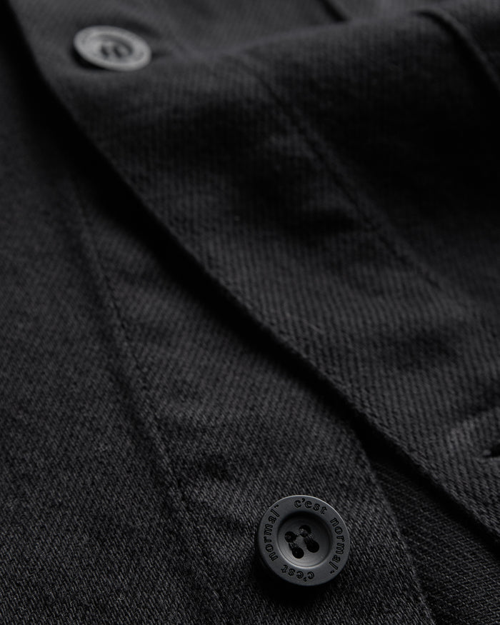 The Workwear Overshirt in black — close-up of the buttons engraved with C'est normal