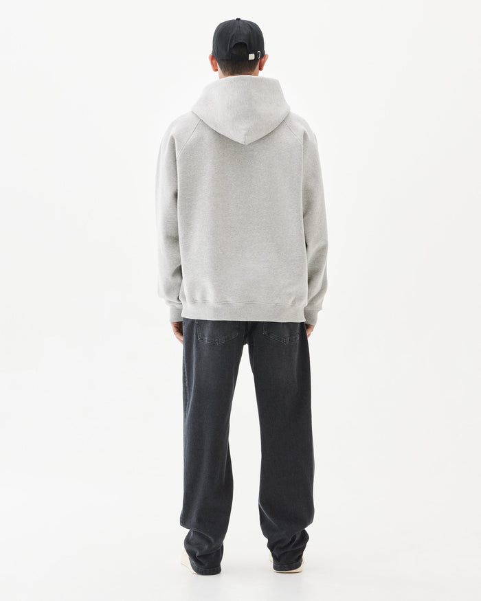 A back view of a person wearing the Tonal Oversized Hoodie in Grey Melange, paired with black jeans and a black cap with a c'est normal tag on the back, standing against a white background.