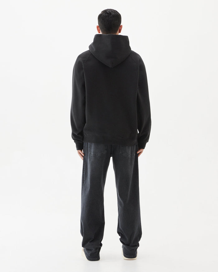 A back view of a man wearing the Tonal Oversized Hoodie in black and dark jeans, standing against a white background.