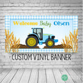 Blue tractor baby shower banner with blue gingham border, golden wheat accents, and Welcome Baby text