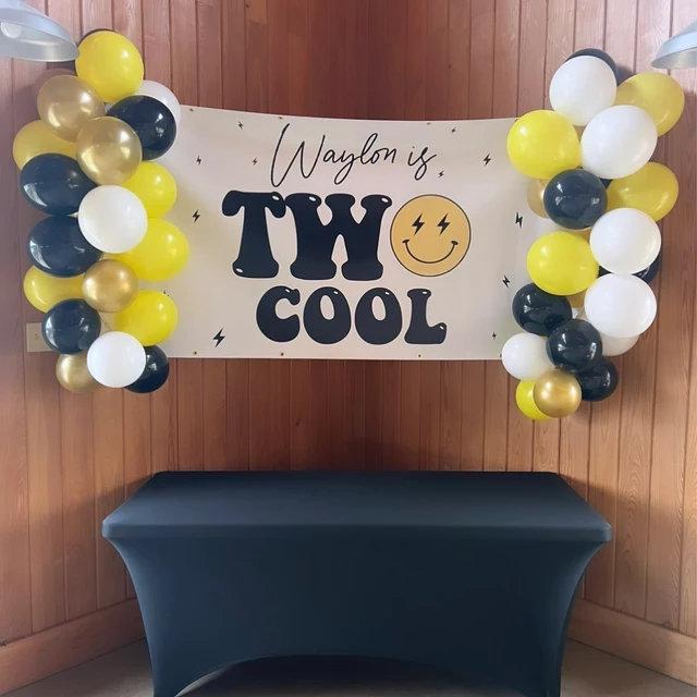 "Modern 'Two Cool' birthday party banner decorated with a smiley face and lightning bolts in a sleek, contemporary style for a second birthday celebration with yellow, gold and white balloon garland