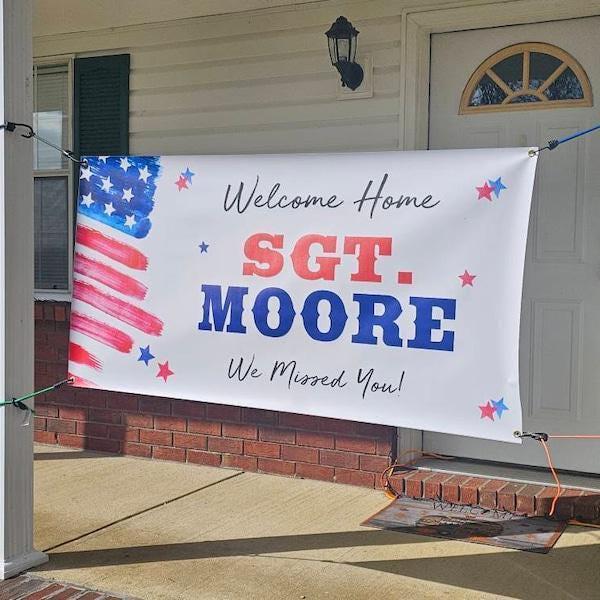 A banner hanging on a porch welcoming home a soldier. The banner features an American flag design and the text "Welcome Home SGT. MOORE We Missed You!"