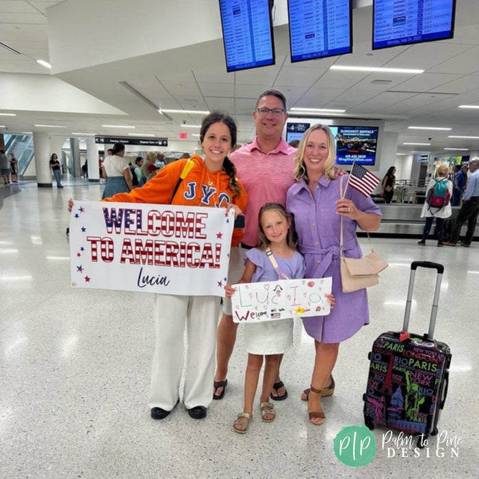A family of four, including two adults and two children, posing for a photo in an airport terminal. They are holding a sign that says "Welcome to America Lucia".