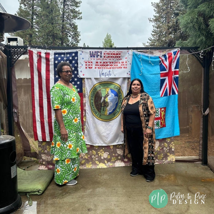 Two women stand in front of a welcome sign with flags of the United States and Fiji, posing for a photo.