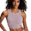 Woman wearing a light purple sports bra and shorts on a plain background