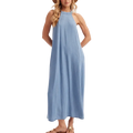 A woman modeling a sleeveless, high-neck, light blue maxi dress with a relaxed, flowing silhouette, paired with a tan straw hat and brown sandals, set against a plain light gray studio background.