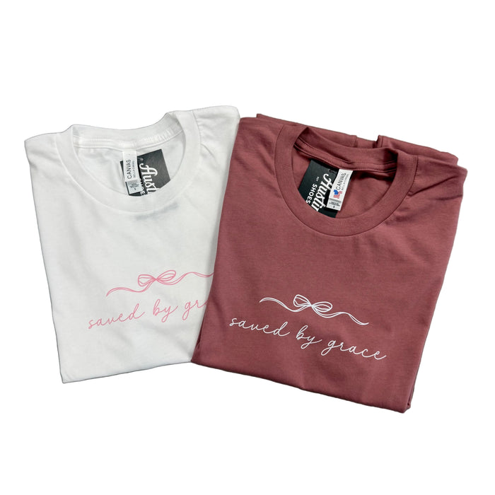Two folded t-shirts, one white and one maroon, with 'saved by grace' text on a white background.